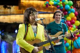 Deux guitaristes en tenues vives et colorées chantent dans des microphones devant une arche de ballons.