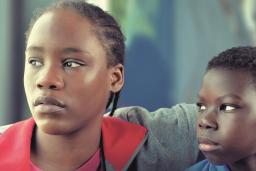 Lokita, une migrante camerounaise de 16 ans, entoure de son bras Tori, un jeune Béninois de 11 ans. Elle regarde ailleurs, l’air tendu et inquiet, tandis qu’il la regarde intensément.