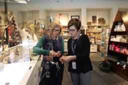 Deux femmes regardent un bijou. Elles sont debout dans un magasin rempli de marchandises colorées.