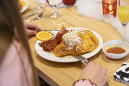 Une personne assise à une table de restaurant mange des gaufres et du bacon.