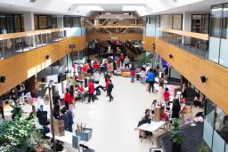 De nombreuses personnes sont rassemblées dans un espace intérieur ouvert où sont disposées des tables et des affiches.