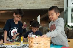 Un enfant plonge dans un panier de matériel de bricolage pendant que d'autres travaillent à leurs projets à une table.