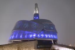  Un édifice recouvert de panneaux de verre illuminé de bleu et de violet. Des motifs de flocons de neige sont également projetés sur les fenêtres.