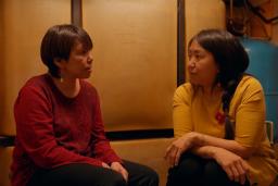 Deux femmes inuites sont assises dans une pièce sombre, l’une en face de l’autre, et discutent de manière intime. L'une porte un chandail rouge, l'autre un chandail jaune.