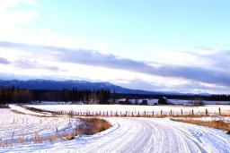 Une route de campagne couverte de neige; on voit des montages au loin.