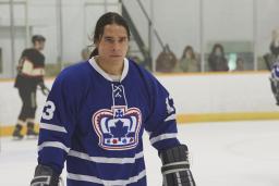 A young man in a blue hockey uniform with a crown logo on an indoor ice rink.