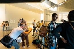 Des projets d’élèves sont exposés sur des chevalets dans une galerie de musée. Deux élèves parlent de leur travail avec des adultes.