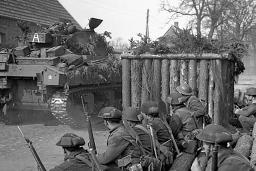 Un groupe de soldats armés regarde passer un char d’assaut.