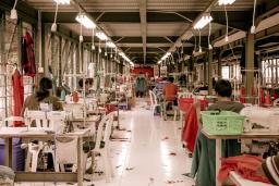 Des travailleuses de l’industrie du vêtement sont assises à des bureaux avec des machines à coudre dans un entrepôt.