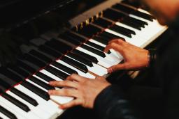 Deux mains jouent sur les touches d’un piano Yamaha d’un noir étincelant. La personne au piano, que l’on voit à peine, porte un haut noir à manches longues.