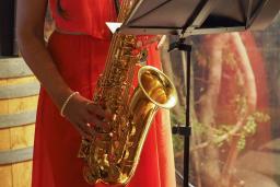 Une musicienne vêtue d’une robe rouge sans manches joue d’un saxophone doré.