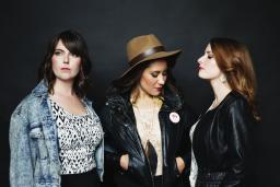 Trois femmes posent devant un mur noir.
