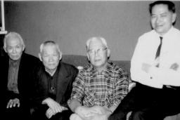 Quatre hommes assis sur un sofa qui regardent l’appareil-photo.