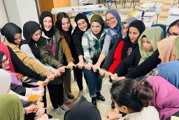 Un groupe de femmes musulmanes souriantes formant un cercle et se tenant par la main.