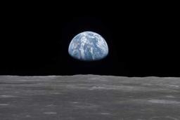 View of earth rising above the lunar horizon, showing the blue and white planet against the dark backdrop of space as seen from the moon’s surface.