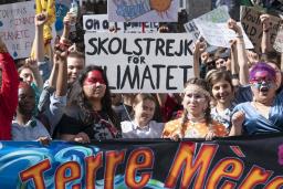 A crowd of youth hold protest signs and stand behind a large banner that reads “La Terre Mère,” or “mother earth” in English.