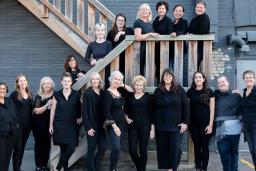 Les membres d’une chorale de femmes sont vêtus de noir et posent le long d’un escalier extérieur en bois.