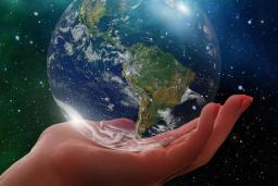 Une image stylisée montre une main humaine tenant délicatement un globe terrestre en verre. L’arrière-plan est un ciel nocturne parsemé d’étoiles et d’aurores boréales d’un vert éclatant.