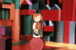 Un bloc de bois, sur lequel est peinte l'image d'un enfant, est posé sur un bloc rond. Des blocs de formes, de couleurs et de tailles différentes apparaissent à l'arrière-plan.