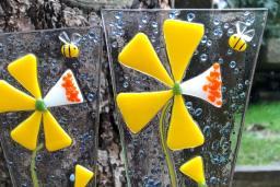 Deux décorations en verre fusionné représentant des fleurs jaunes sont placées dans un pot à fleurs à l’extérieur.
