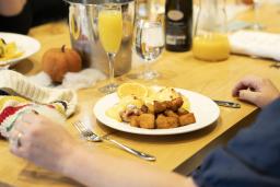 Une personne est assise à une table avec un verre de jus d’orange et une assiette d’œufs bénédictine et de pommes de terre rissolées.