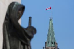 Un drapeau canadien flotte au sommet d’une grande tour. Au premier plan se dresse la statue d’une femme voilée portant une épée.