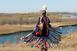 Une danseuse autochtone vêtue d’un châle d’apparat aux couleurs vives, près d’une rivière.