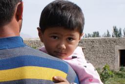 Un jeune enfant porté par un adulte regarde en arrière par-dessus l’épaule de l’adulte.