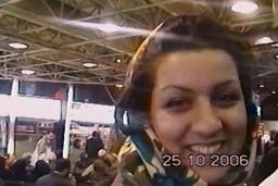 Une jeune femme souriante portant un foulard se tient dans une foule. L’image est datée : 25-10-2006.