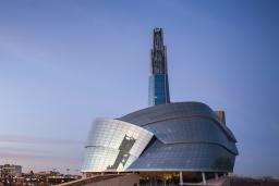 L'extérieur du Musée canadien pour les droits de la personne, vu au coucher du soleil sur la ligne d'horizon de la ville.