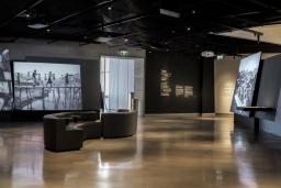 Une galerie de musée où on voit des photographies projetées sur de grands écrans. Il y a des fauteuils au milieu de la pièce.