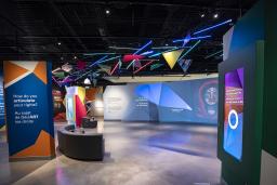 Une galerie de musée où on voit des oeuvres d'art projetées sur de grands écrans et formes géométriques colorées.