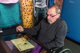Un homme d'un certain âge est assis dans un fauteuil roulant devant un comptoir équipé d'un grand écran tactile.