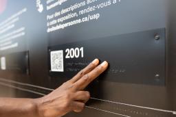 Une main touche des lettres en braille dans une exposition muséale.