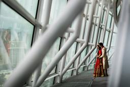 Un homme enlace une femme par derrière alors qu'ils se tiennent ensemble en regardant par un mur de fenêtres soutenu par une grande structure en acier blanc.