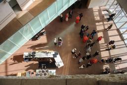 Une vue à vol d'oiseau d'une foule de personnes rassemblées dans un grand espace ouvert du Musée. Il y a quatre tables de cocktail recouvertes de nappes rouges et un bar sur le côté gauche de l'image.
