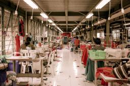 Des travailleuses de l’industrie du vêtement sont assises à des bureaux avec des machines à coudre dans un entrepôt.