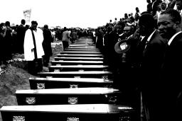 Des gens se tiennent devant une rangée de cercueils.