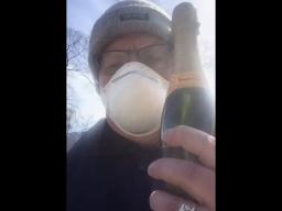 Un homme portant une tuque et un masque respiratoire jetable et tenant une bouteille de vin mousseux.