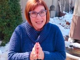 Une femme rousse portant une veste bleue, assise dans un jardin enneigé.