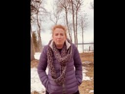 Une femme en manteau d'hiver se tient dehors dans un parc partiellement enneigé.