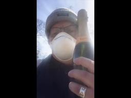 Un homme portant une tuque et un masque respiratoire jetable et tenant une bouteille de vin mousseux.