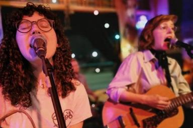 Deux femmes portant des lunettes et des chemises blanches chantent et jouent de la guitare.