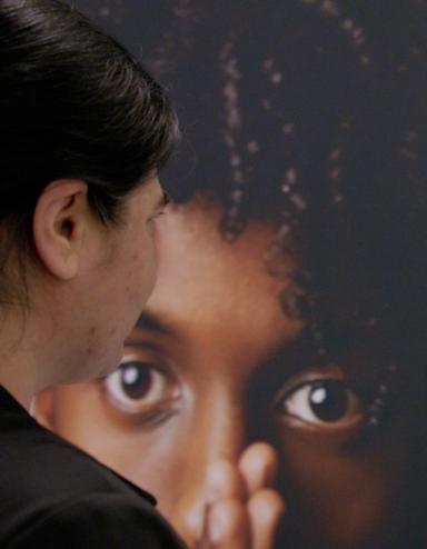 A woman gazes at a display showing faces of a diverse group of people. Visibilité masquée.