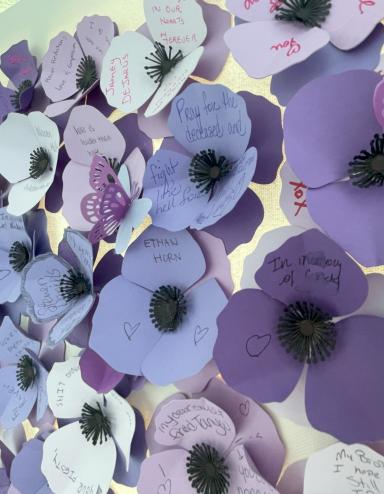 Des pavots violets faits de papier avec des noms et des messages écrits par des membres de la communauté ou de la famille de personne décédées après avoir consommé des drogues empoisonnées. Visibilité masquée.