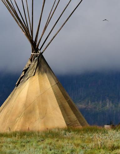 Un grand tipi dans un champ d’herbe. Les perches du tipi s’élèvent dans le ciel brumeux. Visibilité masquée.