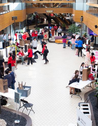 De nombreuses personnes sont rassemblées dans un espace intérieur ouvert où sont disposées des tables et des affiches. Visibilité masquée.