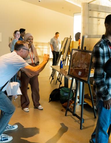 Des projets d’élèves sont exposés sur des chevalets dans une galerie de musée. Deux élèves parlent de leur travail avec des adultes. Visibilité masquée.