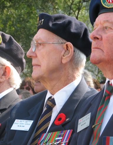 Trois hommes âgés, membres de la Légion canadienne, sont assis côte à côte. Tous les trois portent le coquelicot du jour du Souvenir sur leur uniforme. Visibilité masquée.