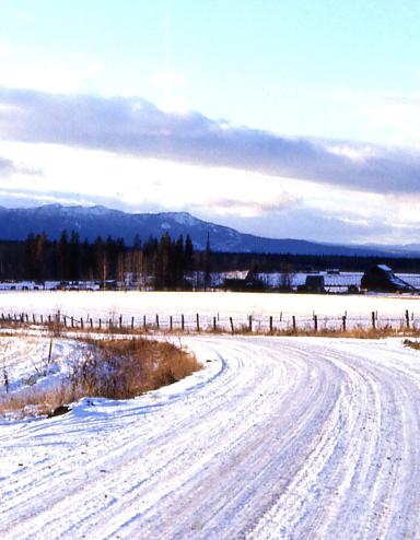Une route de campagne couverte de neige; on voit des montages au loin. Visibilité masquée.